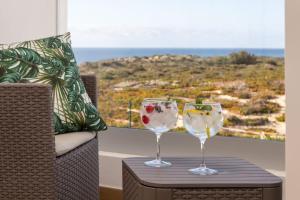 two wine glasses sitting on a table in front of a window at Alojamento White Rose Boutique in Zambujeira do Mar