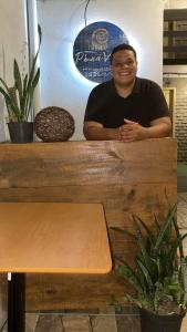a man sitting behind a wooden table with a bench at Pé na Villa in Itacaré