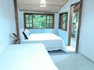 a bedroom with a bed and two windows at Loft 01 encanto dos ipês in Paraty