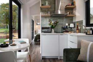 a kitchen with white cabinets and a table and a dining room at Piccola Verde Tiny House in Hepburn
