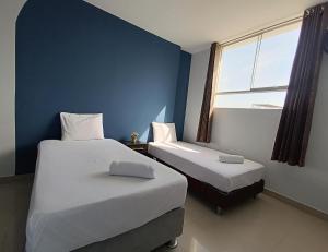 two beds in a room with blue walls and a window at Barlovento Business Hotel in Piura