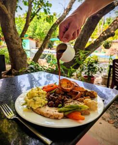 Ein Teller mit Essen steht auf einem Tisch, eine Person gießt Soße darüber. in der Unterkunft Bohemiaz Resort and Spa Kampot in Kampot