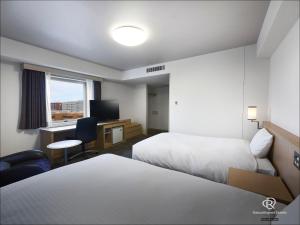 a hotel room with two beds and a desk with a computer at Daiwa Roynet Hotel Hakata-Gion in Fukuoka