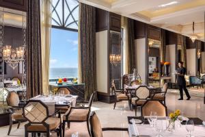 a restaurant with tables and chairs and a man standing in front of a window at The Leela Palace Chennai in Chennai