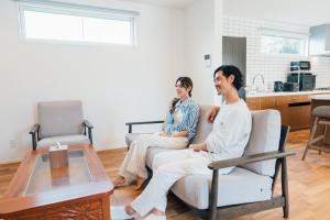 two people sitting on a couch in a living room at Villala Fibana in Motobu