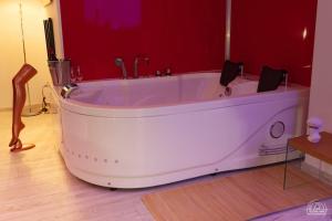 a white tub in a room with a red wall at LoveRoom Les Folies Douces & Spa in Nancy +4 photos