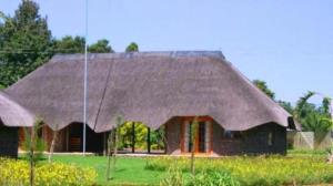 a house with a thatched roof in a field at African Flair Country Lodge in Piet Retief