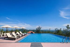 a swimming pool with chairs and umbrellas on a resort at Astralis Resort Coorg in Madikeri