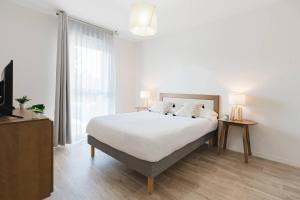 a white bedroom with a bed and a large window at Quality Aparthotel Dinan in Dinan