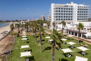 ein Strand mit weißen Sonnenschirmen und Palmen und einem Gebäude in der Unterkunft Palm Beach Hotel - Mehadrin Kosher suitable for Ultra-Orthodox guests in Akkon