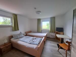 a bedroom with two beds and a desk and a television at Pension Sochor in Aidenbach