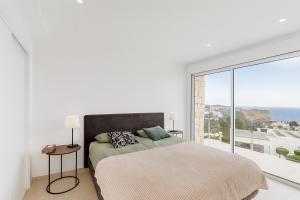 a white bedroom with a bed and a large window at Lirios 182 Cumbre del Sol in Benitachell