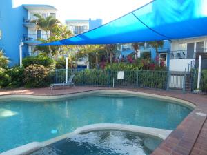 a swimming pool with a blue umbrella next to a building at Tranquil Shores in Caloundra