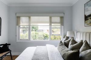 a white bedroom with a couch and two windows at Corner Cottage Bright in Bright