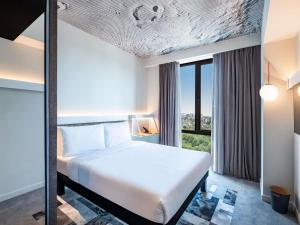 a bedroom with a white bed and a large window at ibis Tbilisi City in Tbilisi City