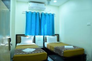 two beds in a room with blue curtains at Ganga Regency in Solapur