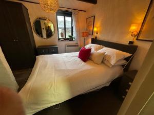 a bedroom with a bed with white sheets and red pillows at Smugglers Cottage converted Barn with Pool & Jacuzzi NR Lyme Regis in Whitchurch Canonicorum