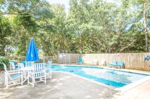 a pool with chairs and a table with a blue umbrella at Seascape Cottage - Kitty Hawk, MP 3.5, 300 Yds to Beach, Pool, Foosball, Near Golf Course, Flex Stays in Kitty Hawk