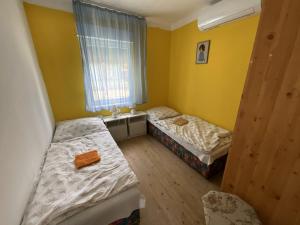 two beds in a room with yellow walls and a window at Anna Vendégház in Harkány