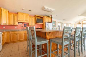 a kitchen with wooden cabinets and a bar with chairs at Dune Diamond - Nags Head MP 16.5, Oceanfront, Elevator, Heated Pool, Hot Tub, Pets OK, Flex Stays in Nags Head +64 photos