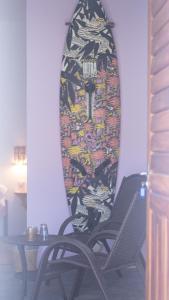 a surfboard on the wall with two chairs and a table at Vila Manguita Suíte Manguita in São Gonçalo do Amarante