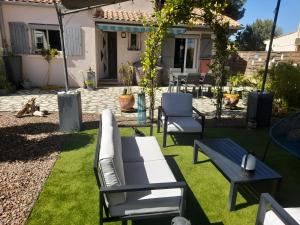 a patio with a white couch and chairs on grass at Chambre double avec balcon in Sérignan