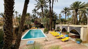 an outdoor swimming pool with chairs and palm trees at Chez Ali Zagora Authentic Hotel Restaurant and Desert Excursions in Zagora