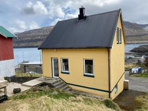 a small yellow house with a black roof at Ocean view from front parquet in Oyndarfjørður