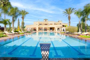 a swimming pool in front of a house with palm trees at Palais les sources de l'atlas, Padel & spa in Marrakesh