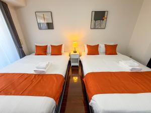 two beds with orange and white sheets in a room at BALCOM STAY Hiroshima Otemachi in Hiroshima