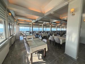 a dining room with tables and chairs and the ocean at Dardanos Yerleşkesi Hotel Eğitim ve Dinlenme Tesisi in Hamidiye