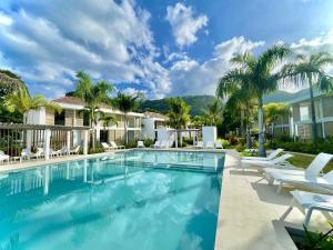 a swimming pool with white chairs and palm trees at Te mana Dream apartment in Paea