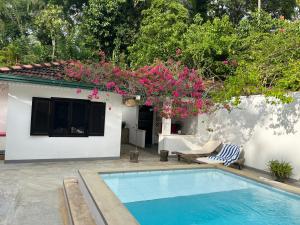 a swimming pool in front of a house with pink flowers at Cinnamon lodge rooms in Koggala