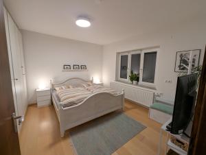 a white bedroom with a bed and a television at Ferienwohnung Erlengrund in Mochenwangen