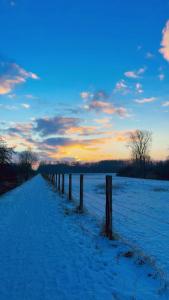 a fence in a snow covered field with a sunset at Le petit paradis de Véro in Nivelle