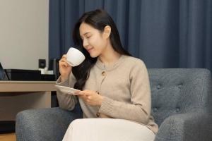 a woman sitting on a couch holding a cup and a cup at H-Avenue Hotel Yeongildae in Pohang
