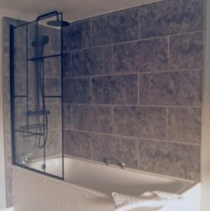 a bathroom with a bath tub with a tile wall at The Old Smithy Bed & Breakfast in Clovelly +23 photos