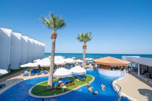 a resort swimming pool with palm trees and the ocean at Mimoza Beach Hotel in Yenibosazici