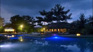 Una piscina de noche con mesas y sombrillas. en Barahi Jungle Lodge, en Meghauli