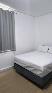 a white bedroom with a bed and a window at Flat Equipado no Centro - Conforto in Governador Valadares
