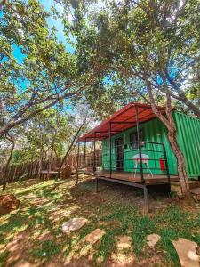 a green house with a red roof under a tree at Cipó Container in Santana do Riacho