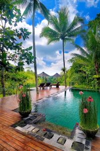 una piscina con palmeras y una terraza de madera en Villa Kalisha - Romantic, Seclusion in the heart of Nature, en Tegalalang