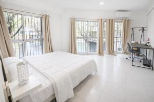 a white bedroom with a bed and a desk and windows at Alicante Beach Hostel in Alicante