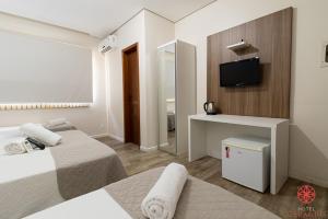 a white room with a bed and a desk and a television at Hotel Geranius Ingleses in Florianópolis