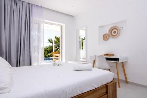a white bedroom with a bed and a desk and a window at serene villas in Ierapetra
