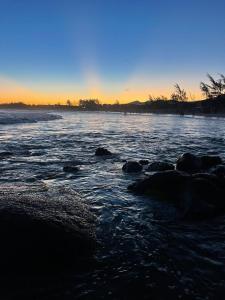 a beach with rocks in the water at sunset at Hospedaria aconchego master in Garopaba +3 photos