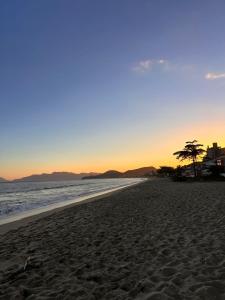 a beach with a tree and the ocean at sunset at Lua Nova Studio II in Caraguatatuba