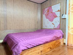 a bedroom with a purple bed with a large painting on the wall at KohLibong Beach House Homestay in Ban Batubute