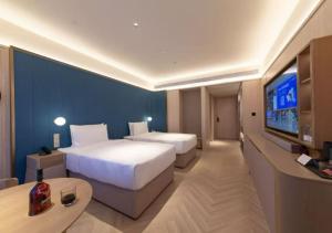 a hotel room with two beds and a flat screen tv at Orange Crystal Hotel Wuhan Jinyinhu in Dongxihu