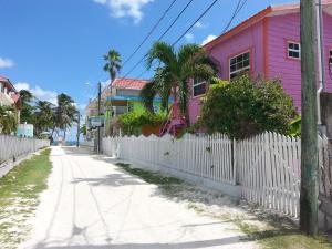 a pink house and a white fence on a street at Sea n sun Guest House in Caye Caulker